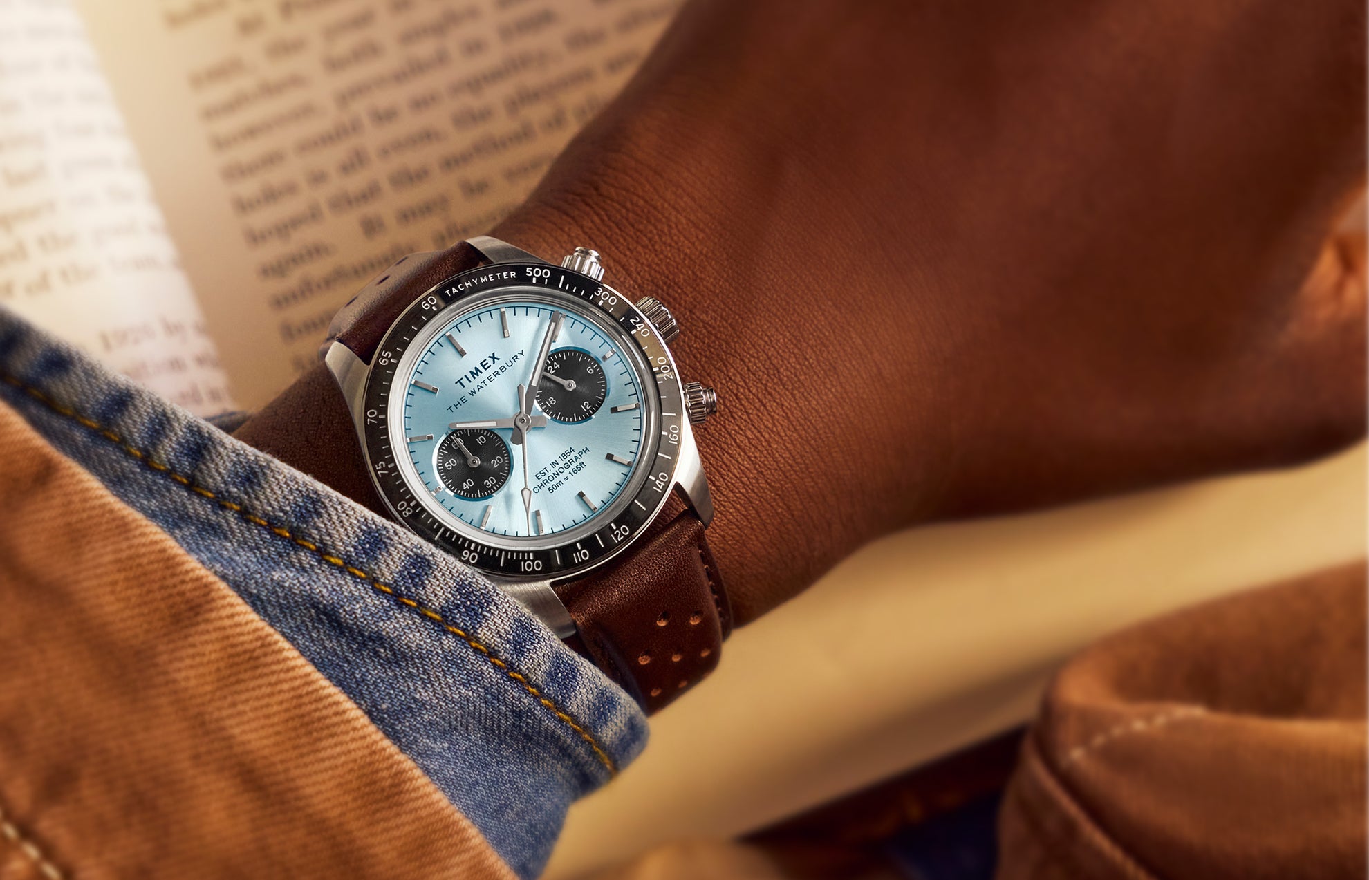 Timex Waterbury Heritage Chronograph worn on wrist with brown leather strap, light blue dial, and black tachymeter bezel.