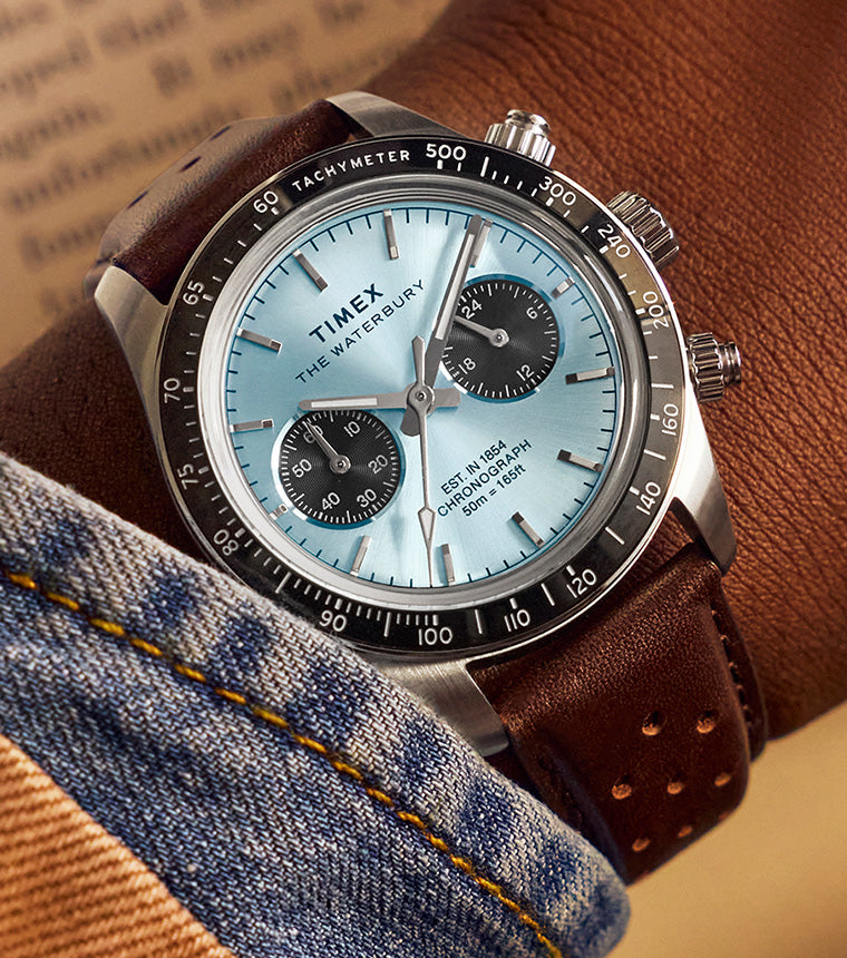 Timex Waterbury Heritage Chronograph worn on wrist with brown leather strap, light blue dial, and black tachymeter bezel.