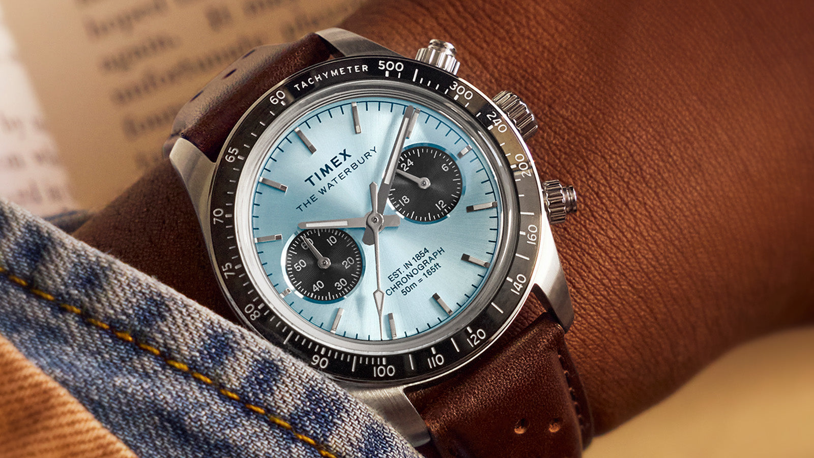 Close-up of Timex Waterbury Heritage Chronograph on wrist, highlighting the light blue dial, chronograph subdials, and leather strap.