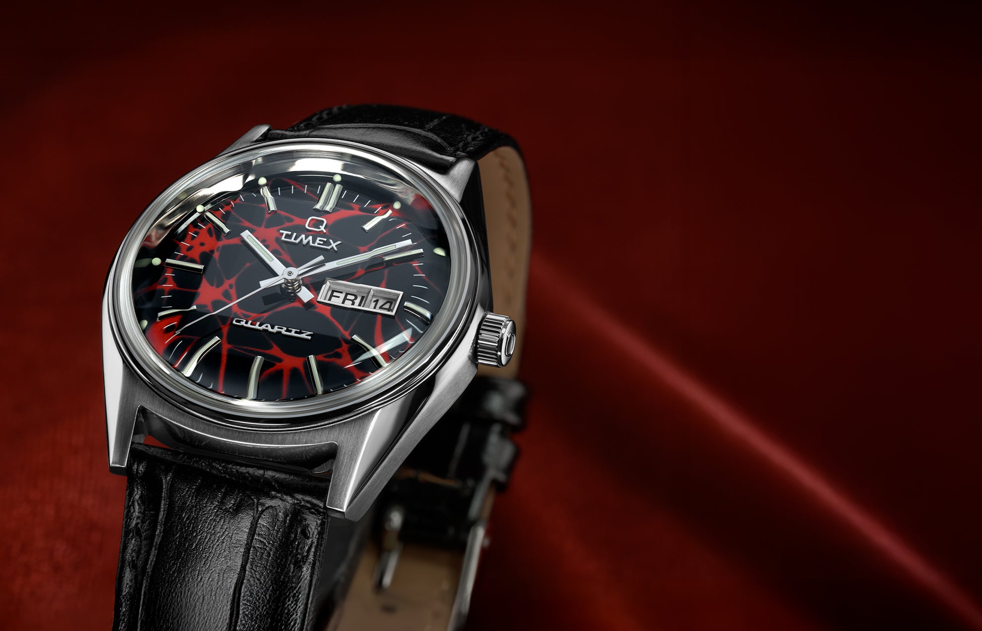 Q Timex® Red Vega 1978 Reissue watch with black leather strap, featuring a red and black patterned dial and stainless steel case on a red fabric background.