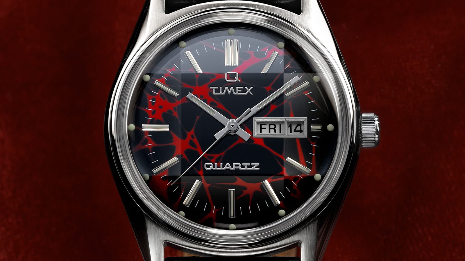 Close-up of the Q Timex® Red Vega 1978 Reissue dial showing the red and black pattern, silver-tone hands, luminous markers, and day-date window.