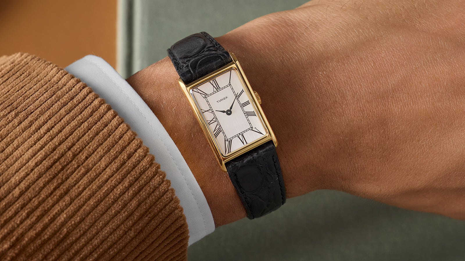 Lifestyle shot of the Timex 1976 Lexington Reissue worn with a brown jacket, showcasing the elegant rectangular case and black leather strap.