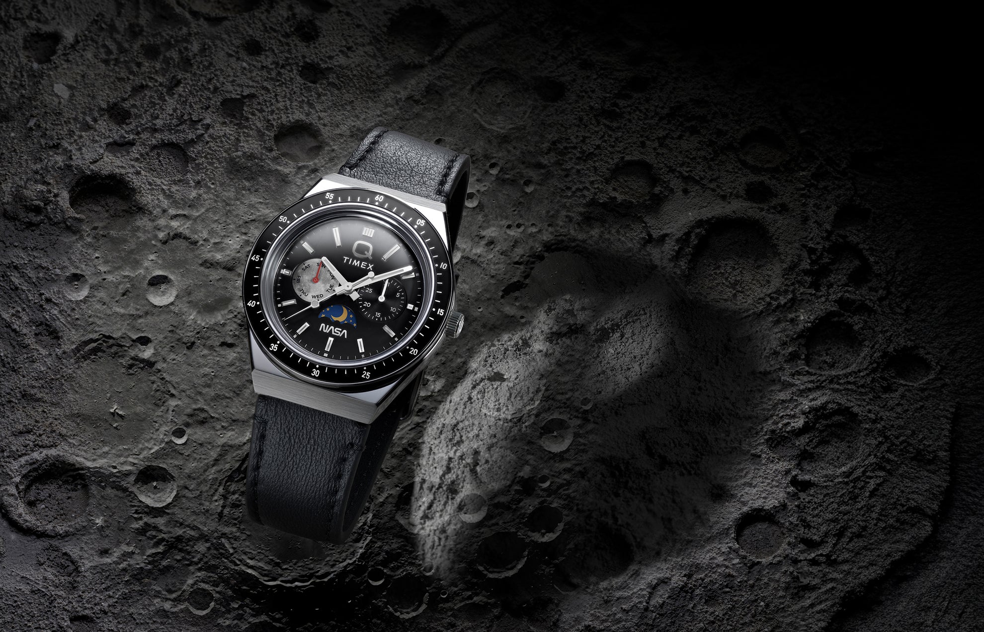 Q Timex® x NASA watch with black leather strap and black bezel displayed against a cratered lunar surface background.