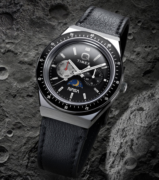 Q Timex® x NASA watch with black leather strap and black bezel displayed against a cratered lunar surface background.