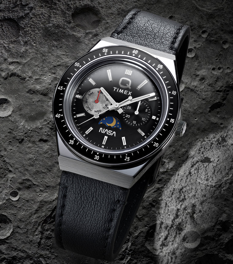 Q Timex® x NASA watch with black leather strap and black bezel displayed against a cratered lunar surface background.
