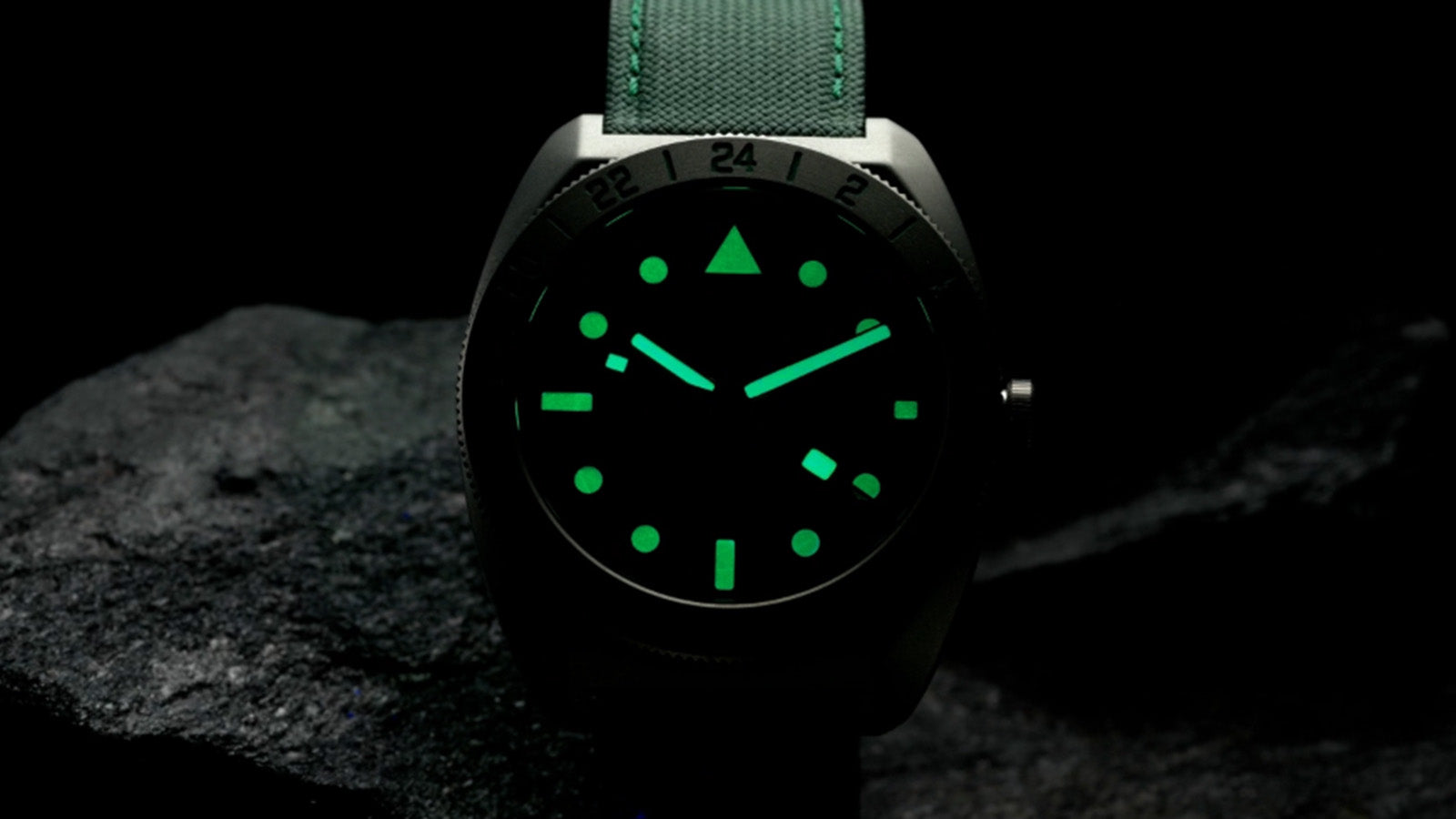 Timex Expedition Pioneer Titanium GMT watch glowing in the dark with bright green luminous hands and markers.