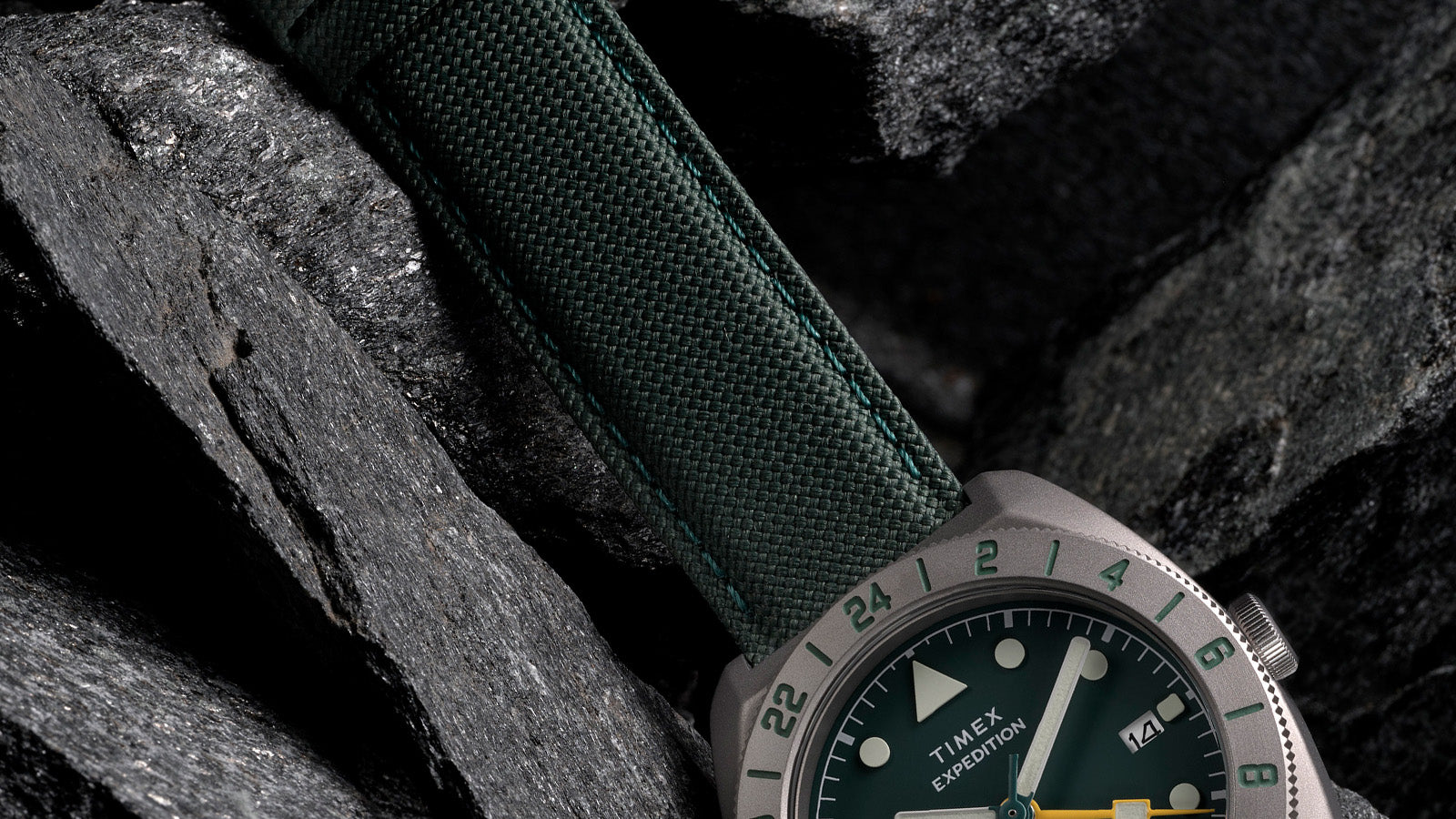 Close-up of green fabric strap and rugged titanium case of Timex Expedition Pioneer GMT watch.
