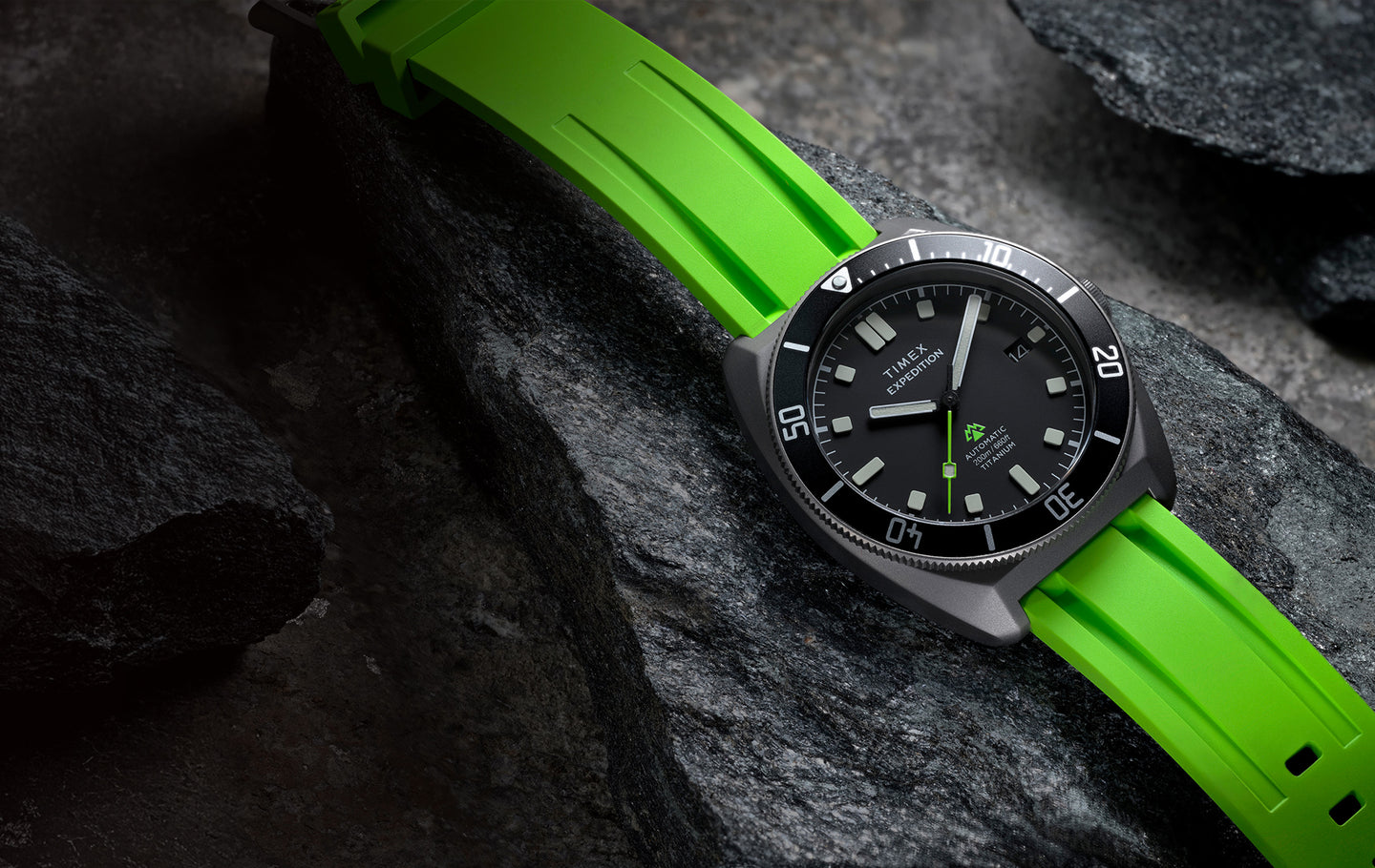 Timex Expedition Pioneer Titanium Automatic watch with a black dial and bright green strap resting on textured dark rocks.