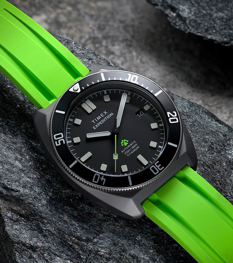 Timex Expedition Pioneer Titanium Automatic watch with a black dial and bright green strap resting on textured dark rocks.
