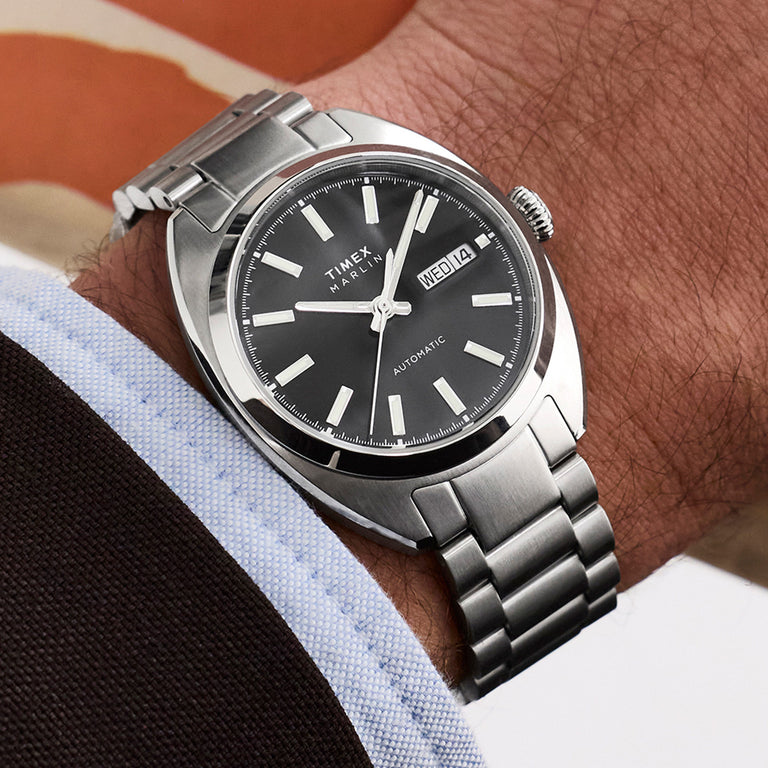 Timex Marlin Draper Automatic watch worn on the wrist, showing a black dial, day-date window, and stainless steel bracelet.