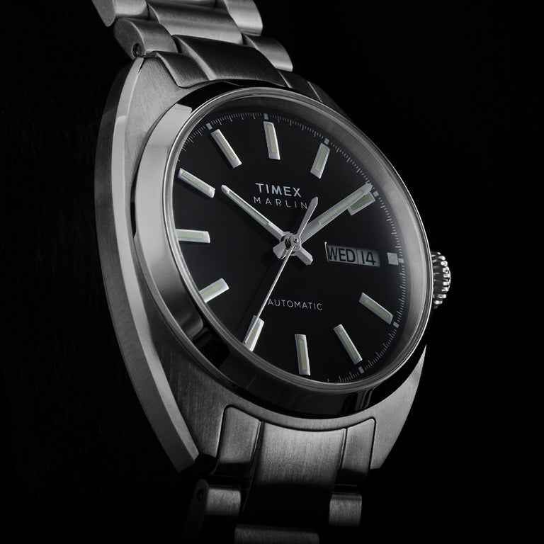 Close-up of the Timex Marlin Draper Automatic black dial with luminous hour markers, silver hands, and day-date display.