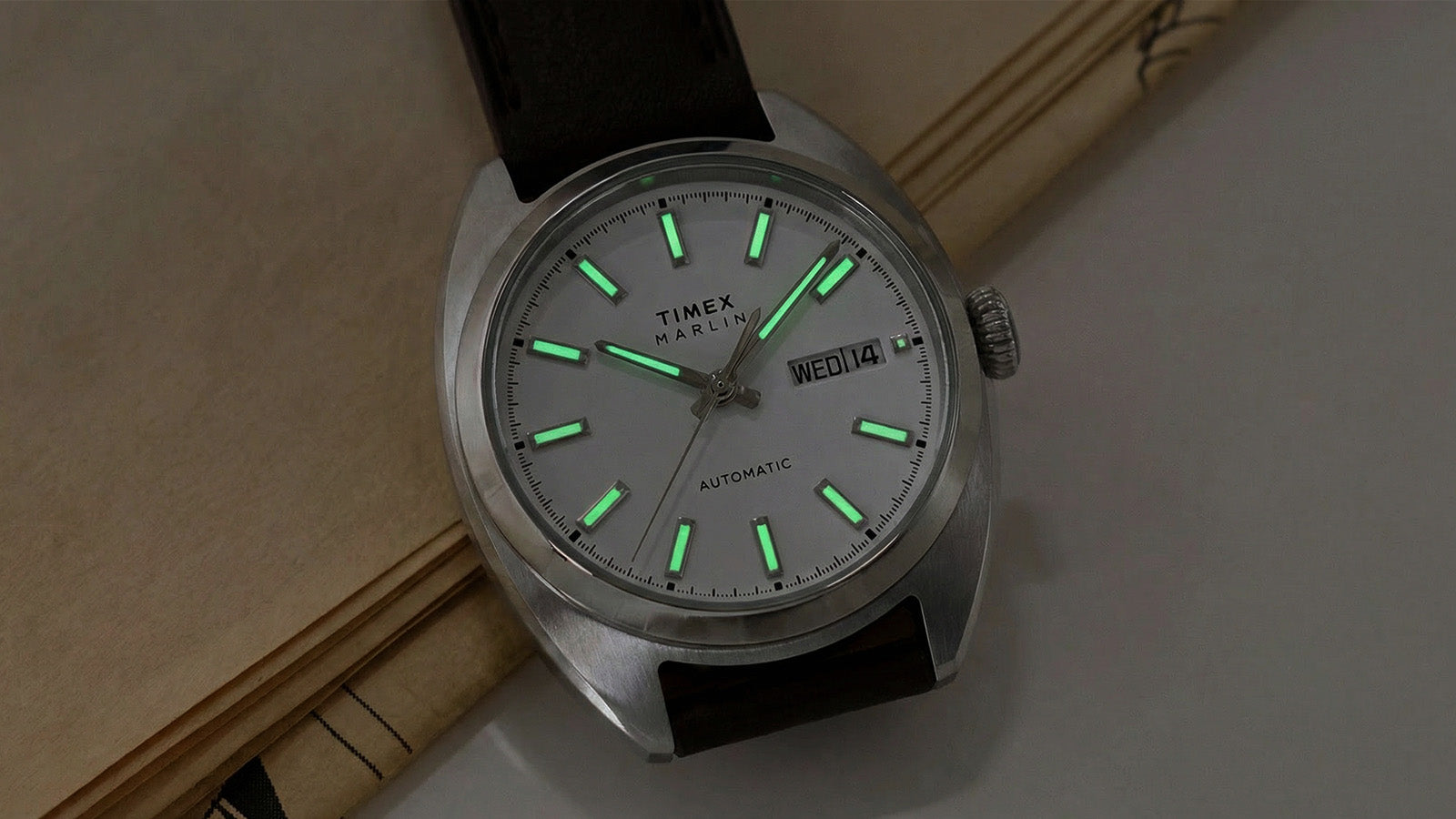 Timex Marlin® Draper Automatic watch with green-glowing luminous hour markers and hands in low light.