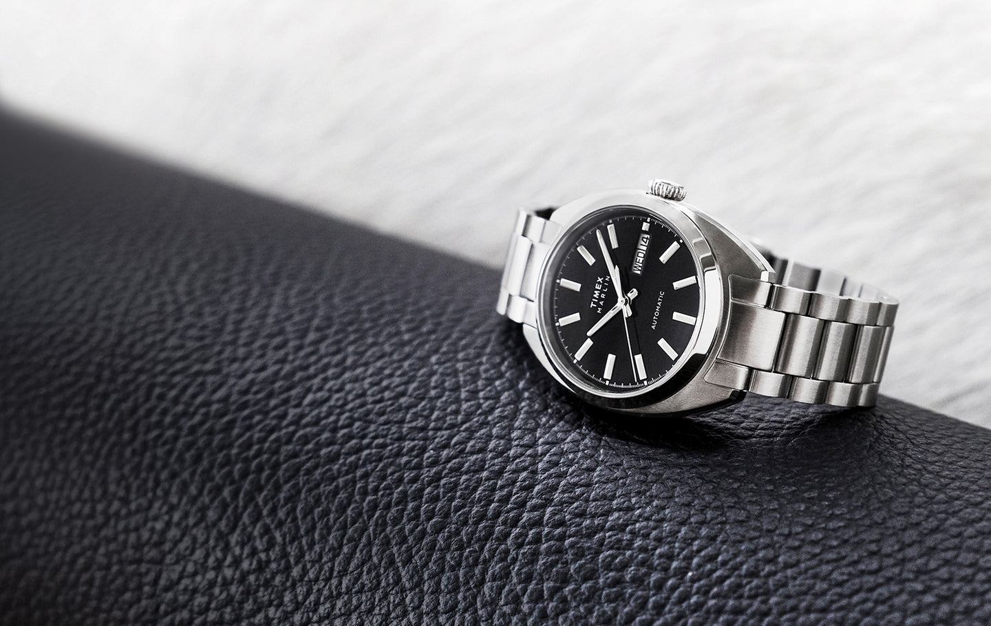 Timex Marlin® Draper Automatic stainless steel watch with black dial and silver bracelet resting on a textured black surface.