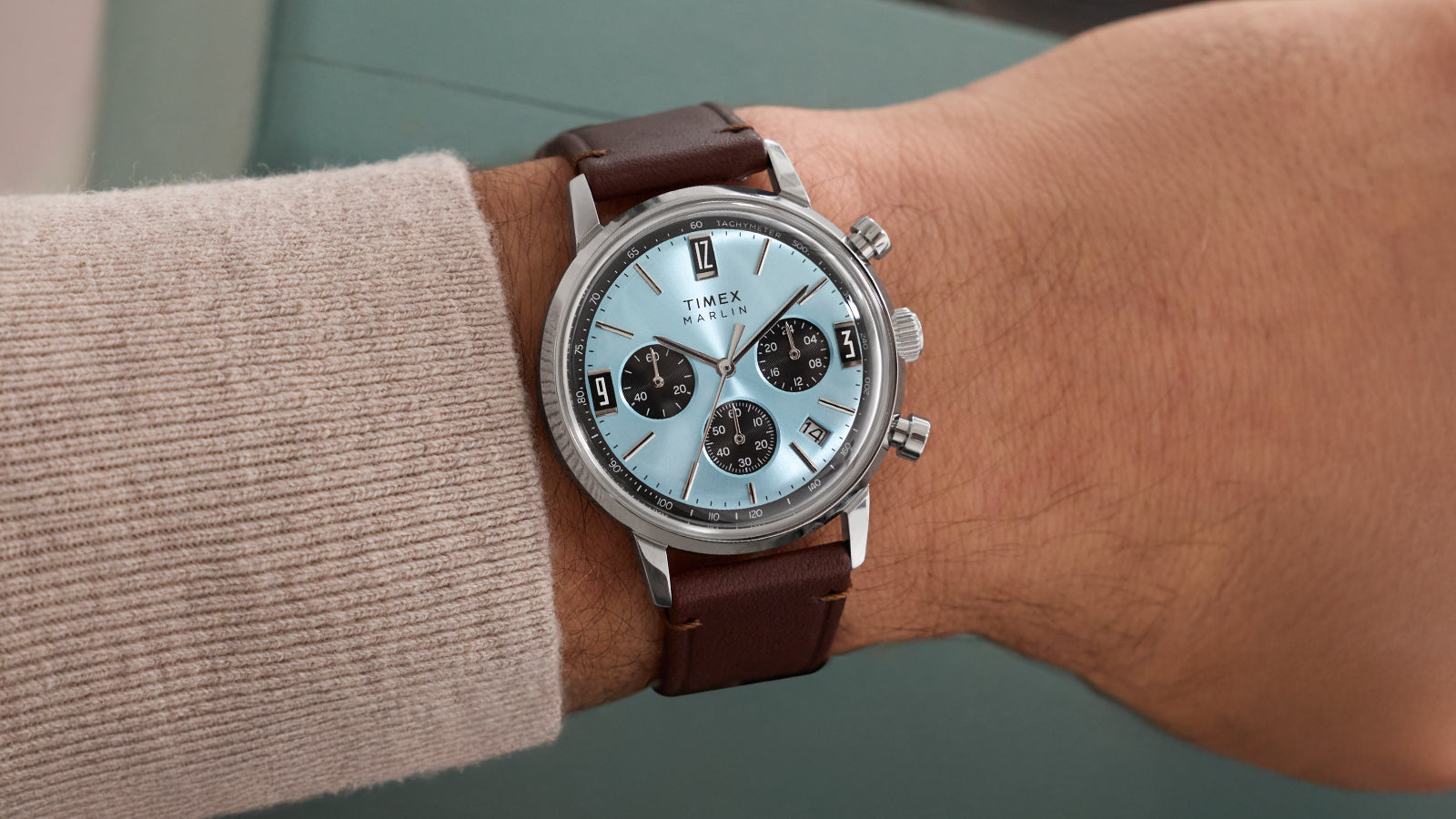 Timex Marlin Chronograph Tachymeter watch with a light blue dial and brown leather strap worn on a wrist, featuring black chronograph subdials and tachymeter scale.