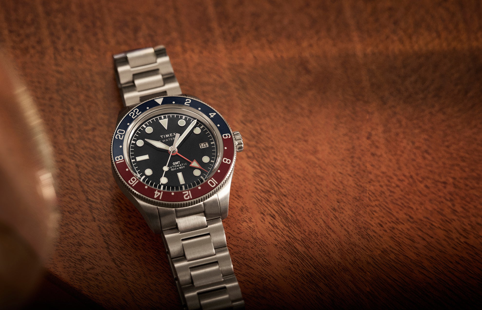 Timex Waterbury GMT automatic watch with stainless steel bracelet and black dial placed on a wooden surface.