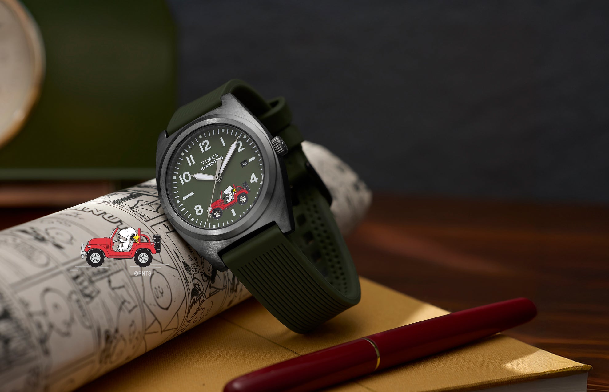 Peanuts® x Timex Expedition Snoopy Road Trip watch with green dial and strap, featuring Snoopy and Woodstock in a red Jeep, resting on an illustrated sketchbook with a red pen nearby.