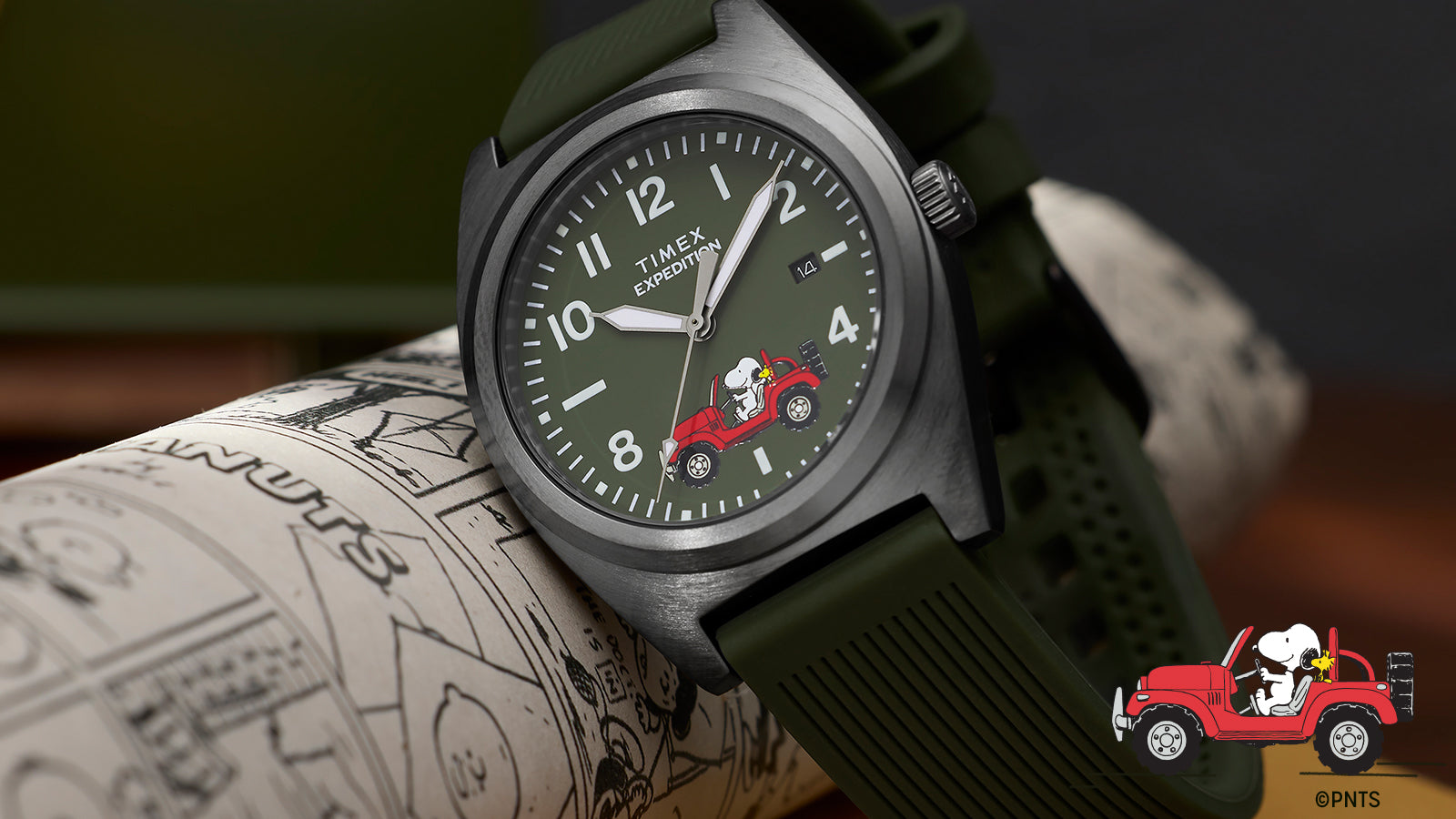 Close-up of Peanuts® x Timex Expedition watch with brushed gray case, green dial, date window, and Snoopy in a red Jeep illustration at 6 o’clock.