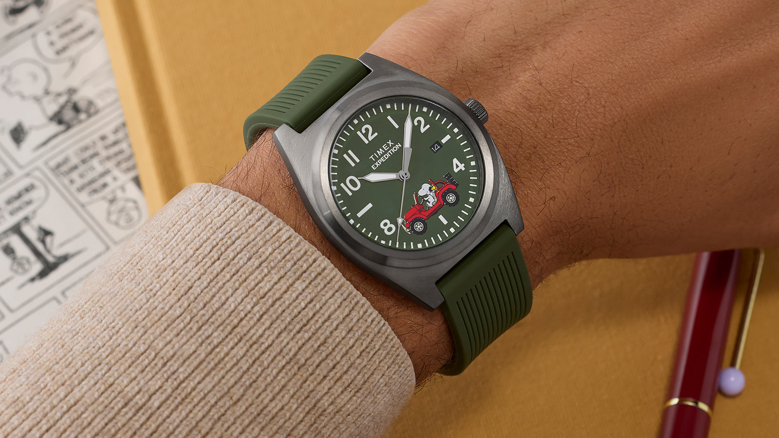 Side angle of Timex Expedition Snoopy Road Trip watch on wrist, featuring matte gray case, green silicone strap, and Peanuts® red Jeep artwork on dial.