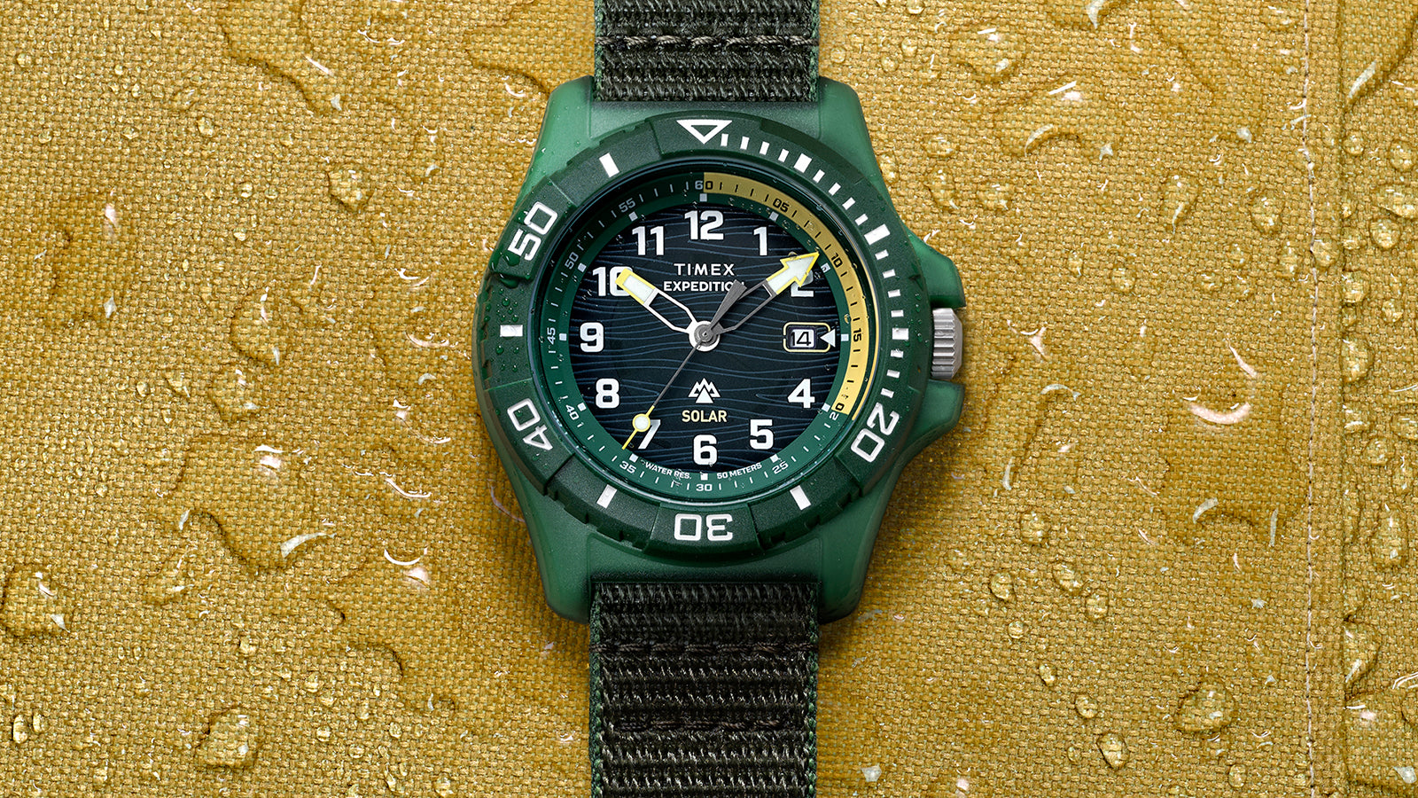 Front view of Timex Expedition® Freedive Solar watch centered on yellow textured surface with visible water droplets and black fabric strap.
