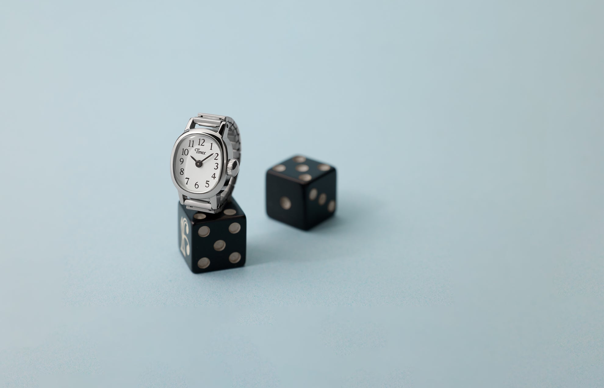 Timex Cavatina® Mini silver-tone watch with white dial displayed on black dice against soft blue background.