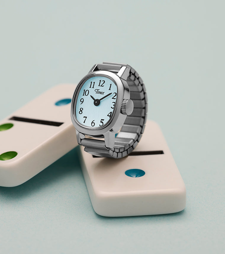 Timex Cavatina® Mini silver-tone watch displayed on white domino blocks against soft blue background.