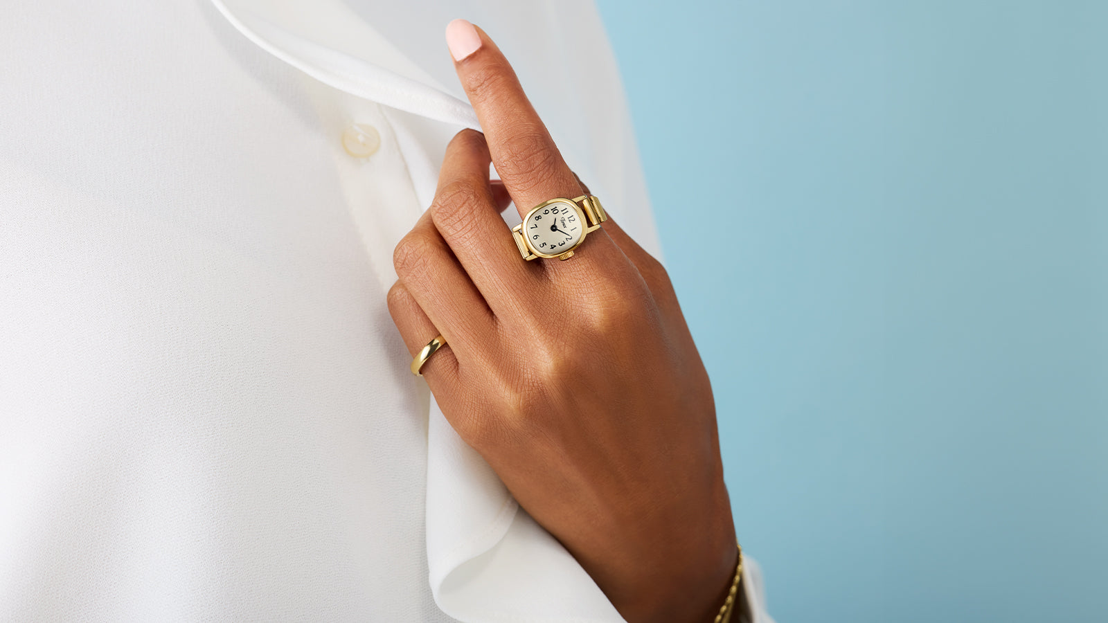 Timex Cavatina® Mini gold-tone watch worn as a ring on finger, paired with white blouse and gold jewelry.