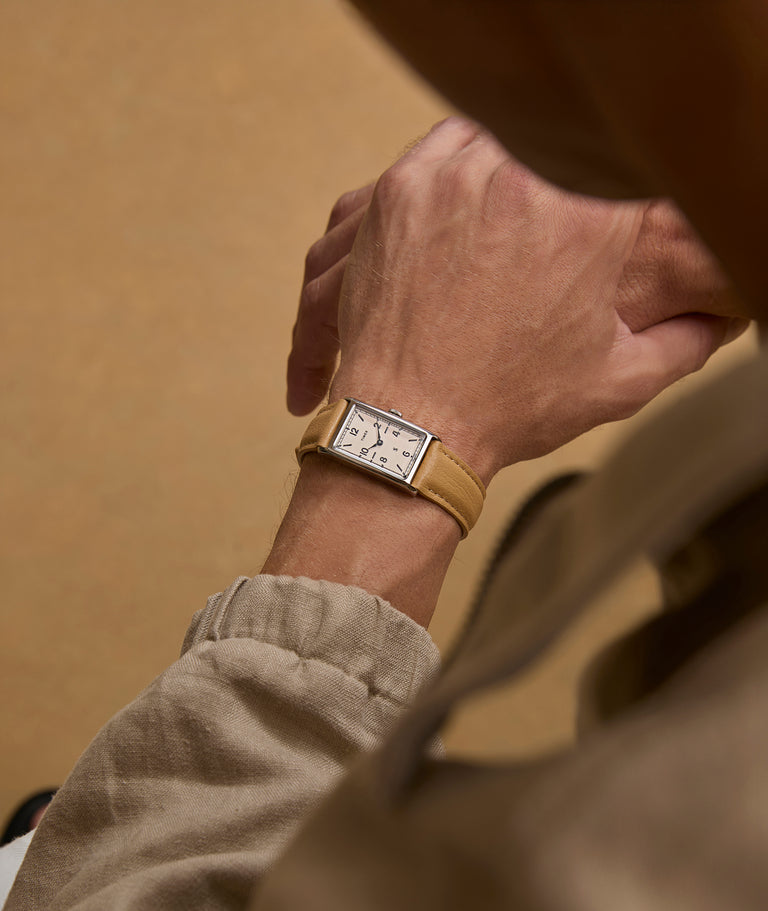 Overhead view of a person wearing a Todd Snyder x Timex 1976 Lexington watch with a rectangular dial and tan leather strap, paired with neutral-toned clothing.