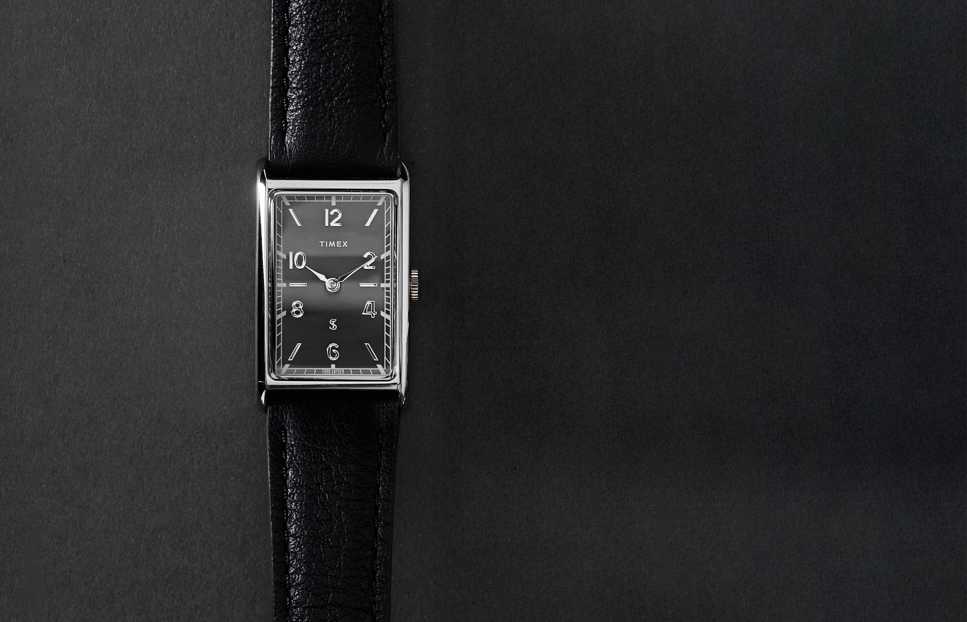 Timex x Todd Snyder 1976 Lexington rectangular watch with a black dial and black leather strap displayed vertically on a dark background