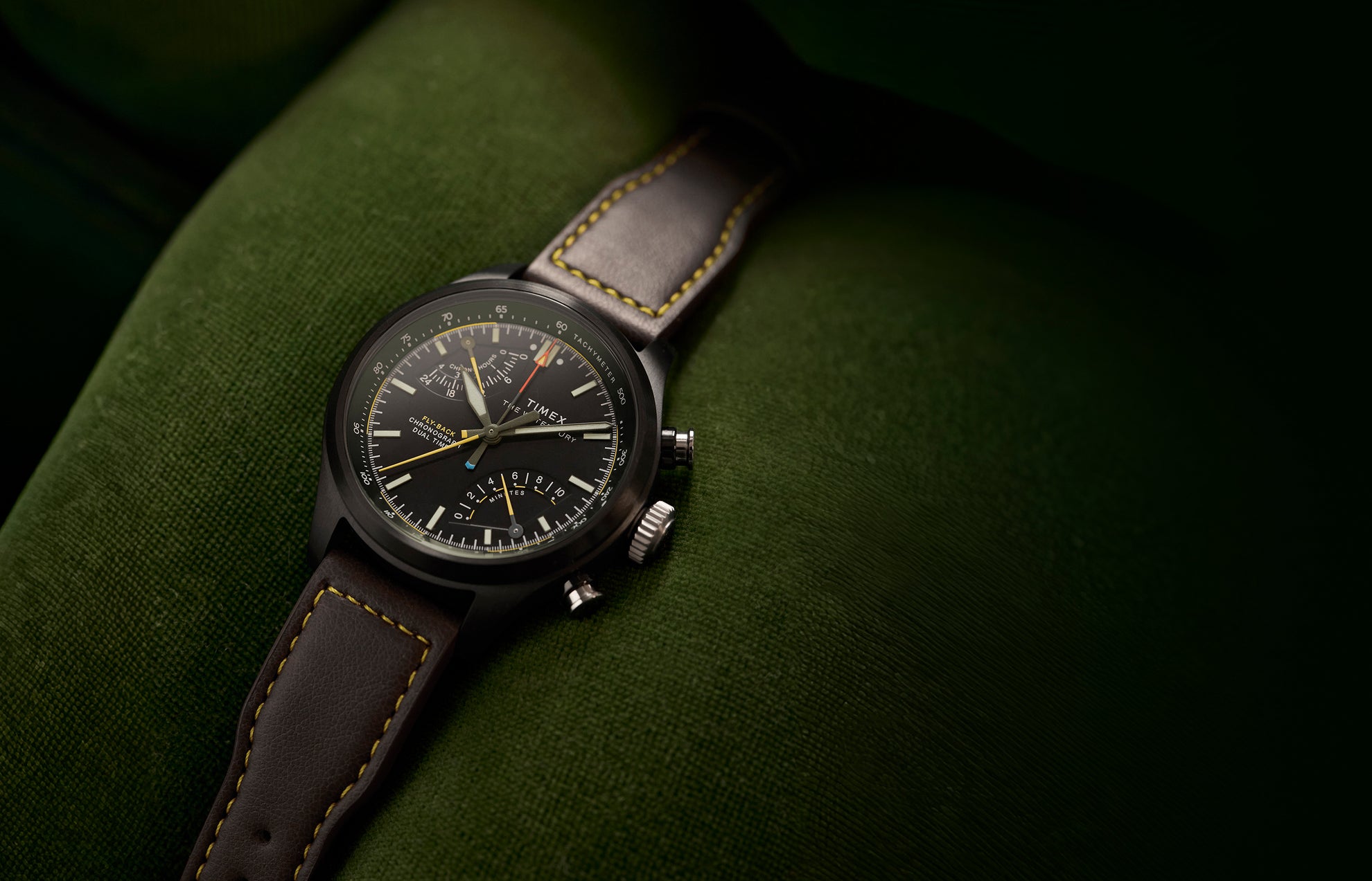 Timex Waterbury Ace Fly-Back Chronograph with black dial and brown leather strap on green fabric surface
