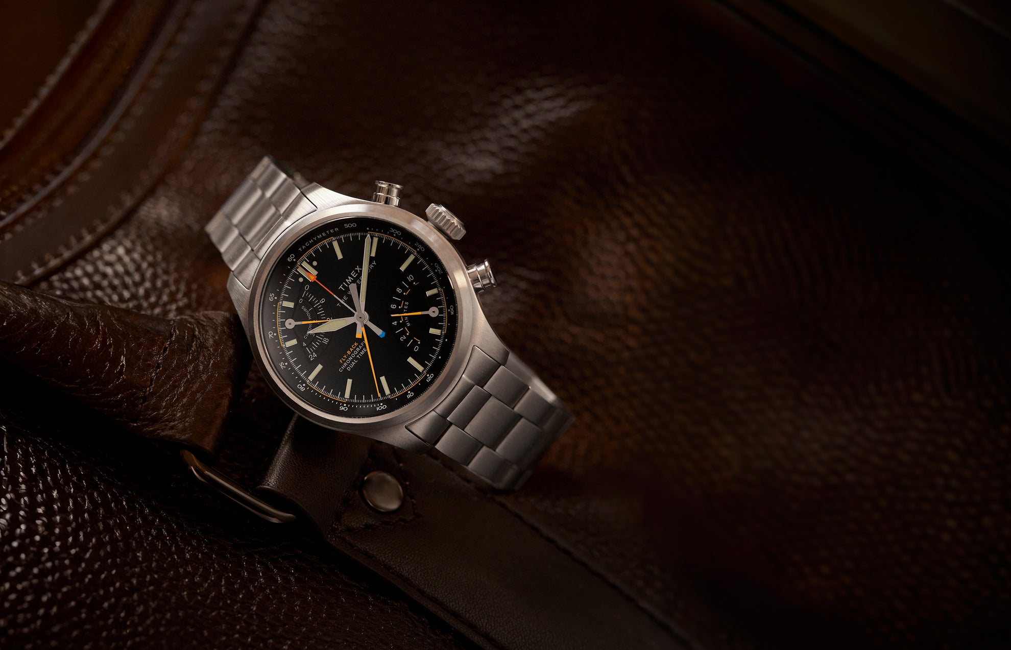 Timex Waterbury Ace Fly-Back Chronograph with black dial and stainless steel bracelet resting on brown leather bag