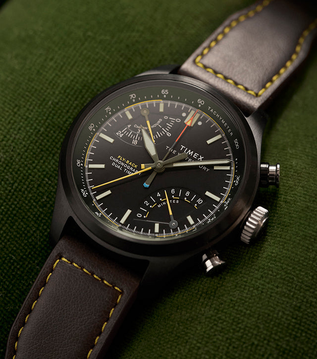 Timex Waterbury Ace Fly-Back Chronograph with black dial and brown leather strap on green fabric surface