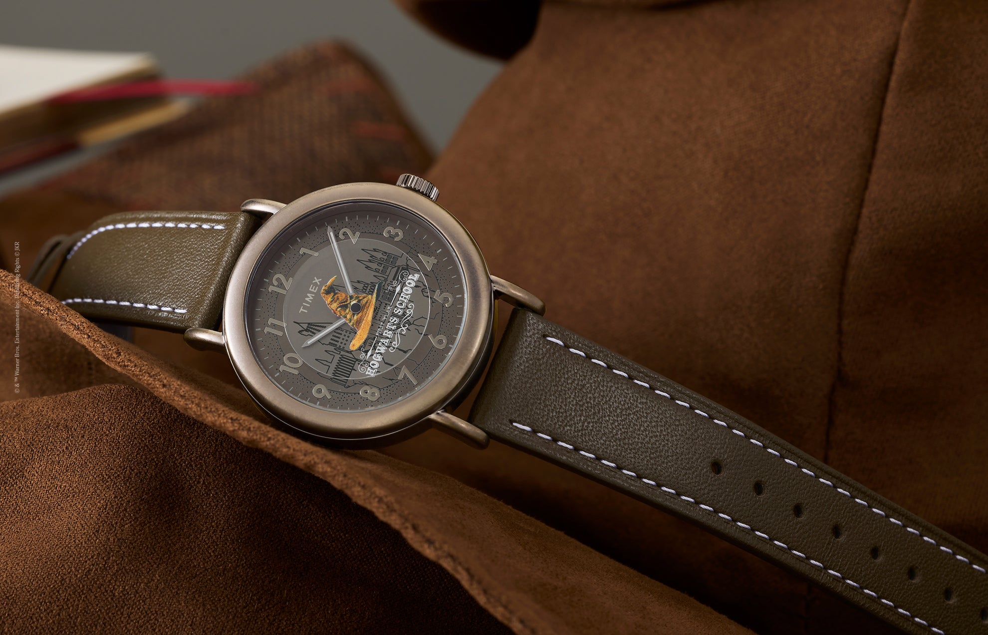 Harry Potter x Timex Weekender Sorting Hat watch with bronze-tone case and brown leather strap resting on leather chair.
