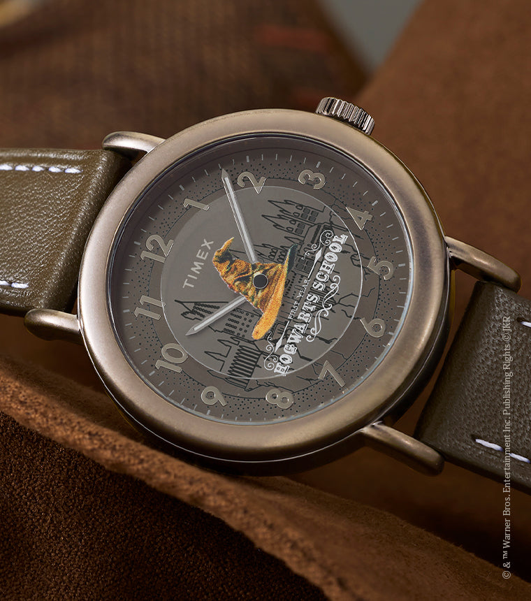 Harry Potter x Timex Weekender Sorting Hat watch with bronze-tone case and brown leather strap resting on leather chair.