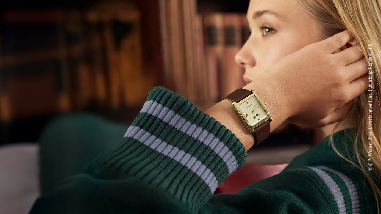 Harry Potter x Timex Hailey Hogwarts watch worn on wrist with gold-tone rectangular case and brown leather strap.