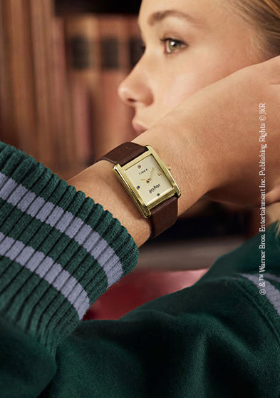 Harry Potter x Timex Hailey Hogwarts watch worn on wrist with gold-tone rectangular case and brown leather strap.