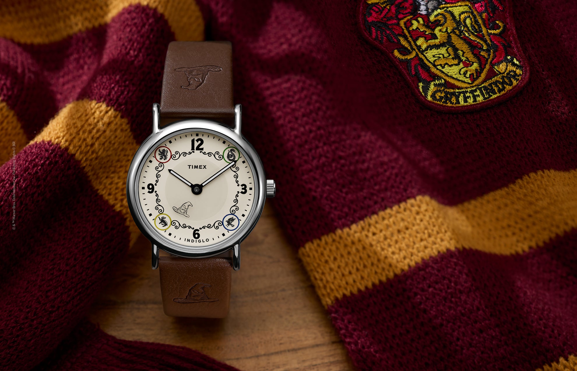 Harry Potter x Timex Weekender Gryffindor House watch with brown leather strap displayed beside a red and gold Gryffindor scarf.