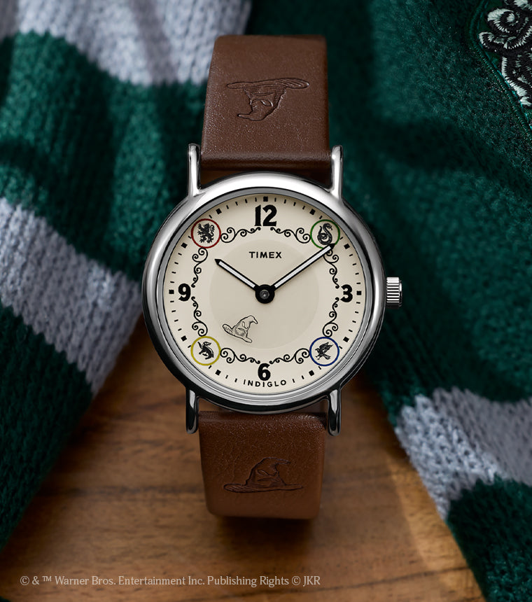 Harry Potter x Timex Weekender Slytherin House watch with brown leather strap displayed beside a green and silver Slytherin scarf.