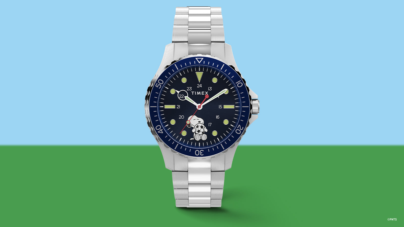 Timex Navi x Peanuts Snoopy soccer watch with blue dial and stainless steel bracelet on blue and green background