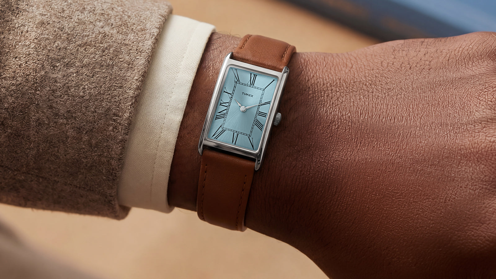 Person wearing the Timex® 1976 Lexington Reissue Inspired watch with a rectangular case, light blue dial, and brown leather strap in a casual setting.
