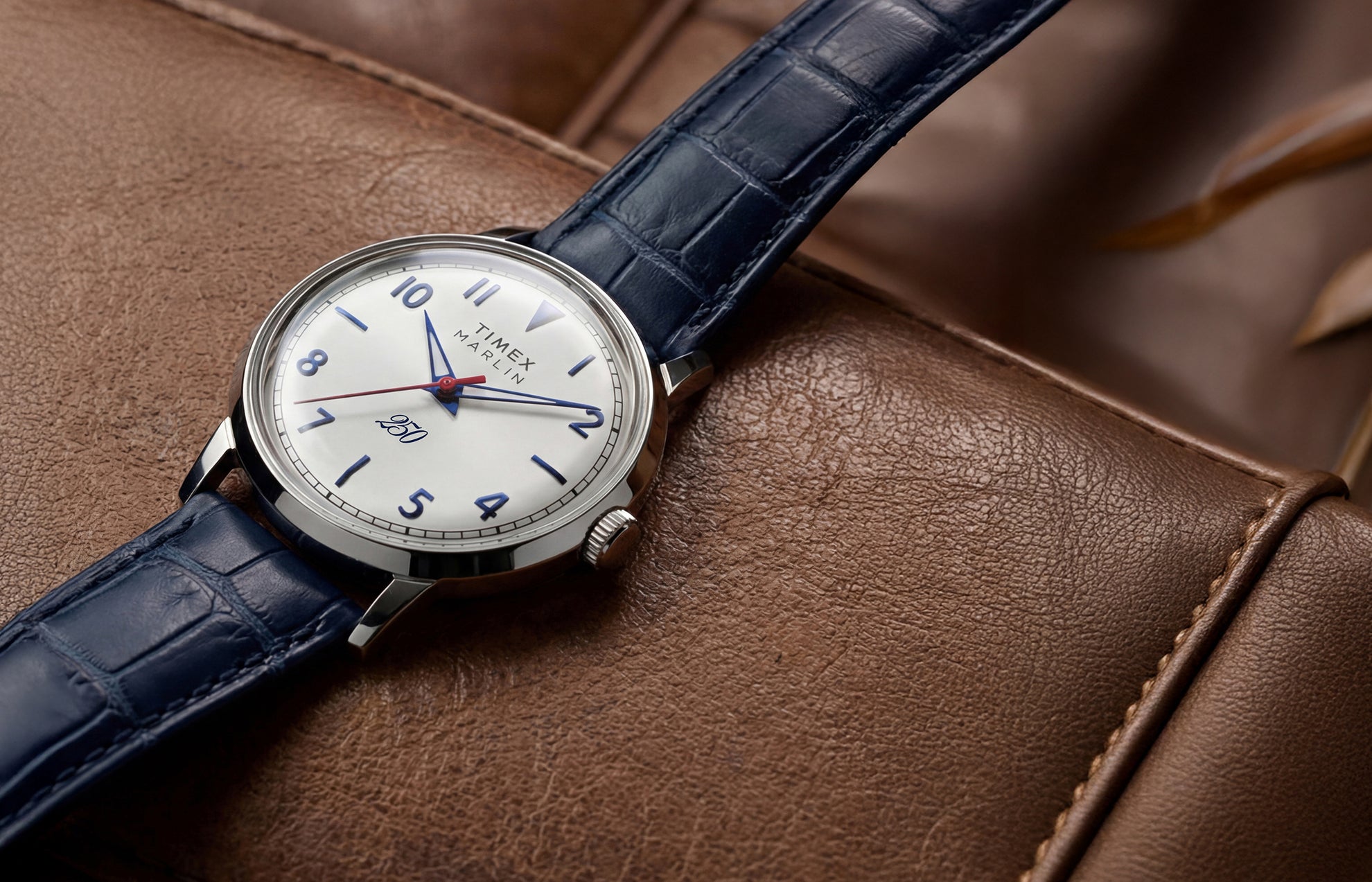 Marlin America 250 watch with a white dial, blue accents, red seconds hand, and blue leather strap displayed on a brown leather surface.