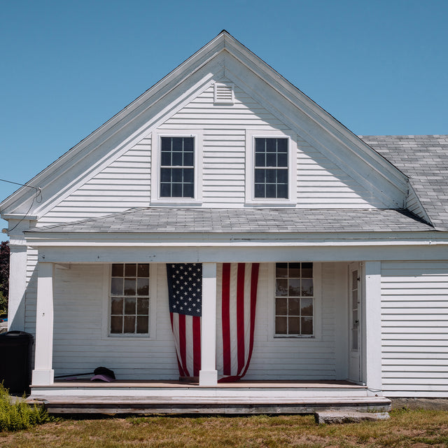 Historic white American home with a U.S. flag displayed on the front porch, reflecting the heritage inspiration behind the Waterbury America 250 Collection.