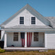 Historic white American home with a U.S. flag displayed on the front porch, reflecting the heritage inspiration behind the Waterbury America 250 Collection.