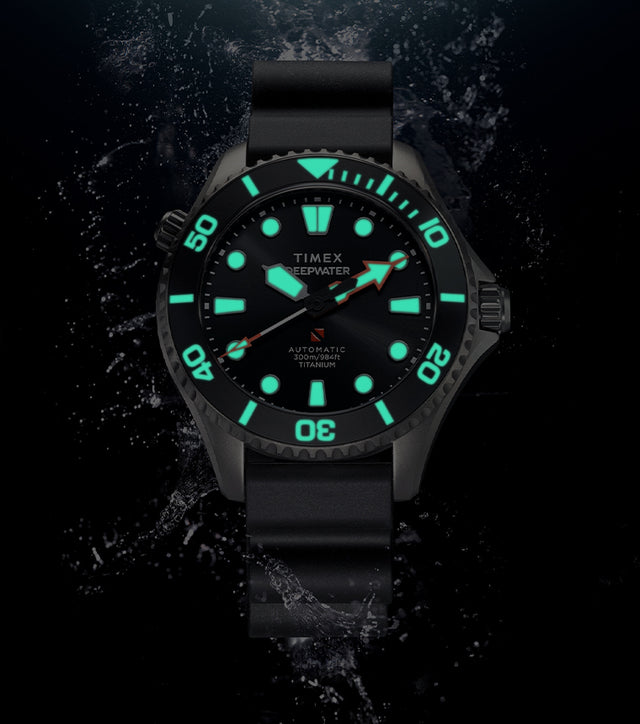 Timex Deepwater Meridian 300 Titanium HEV Automatic dive watch displaying bright blue-green Super-LumiNova illumination against a dark underwater-inspired background.