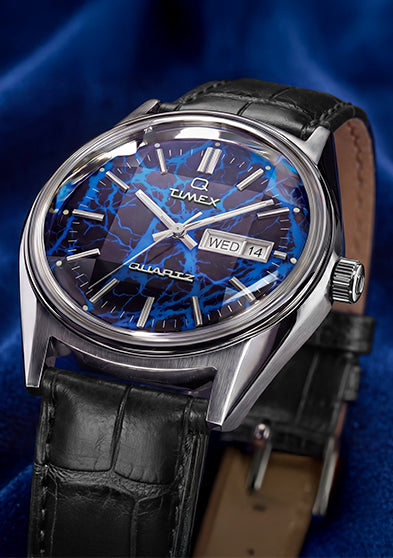 Angled hero shot of Q Timex Blue Vega quartz watch featuring brushed stainless steel case, blue lightning dial, and black crocodile-grain leather strap