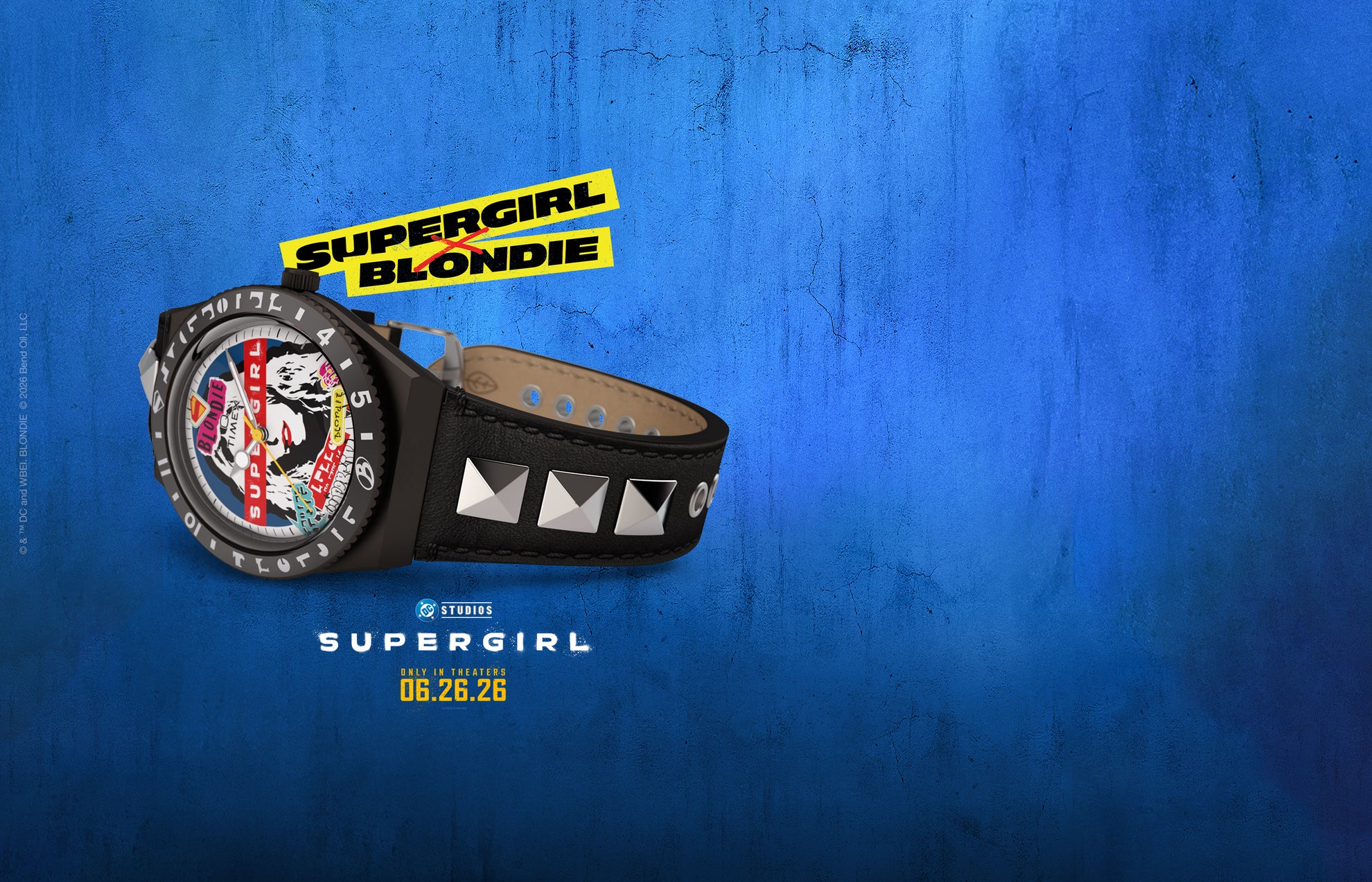 Q Timex x Supergirl x Blondie watch displayed against a textured blue background, featuring a collage-style Blondie portrait dial, black case, and black leather strap with silver pyramid studs. Supergirl Blondie collaboration logo appears above the watch, with the Supergirl movie release date below.