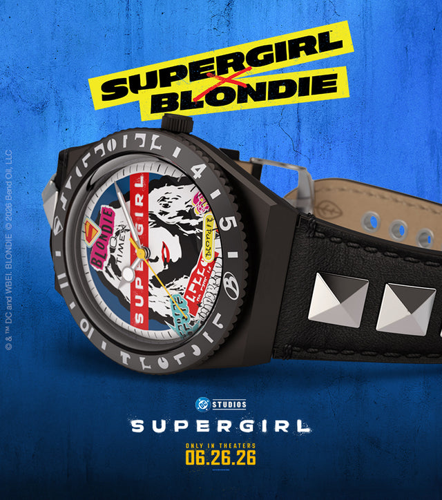 Q Timex x Supergirl x Blondie watch displayed against a textured blue background, featuring a collage-style Blondie portrait dial, black case, and black leather strap with silver pyramid studs. Supergirl Blondie collaboration logo appears above the watch, with the Supergirl movie release date below.