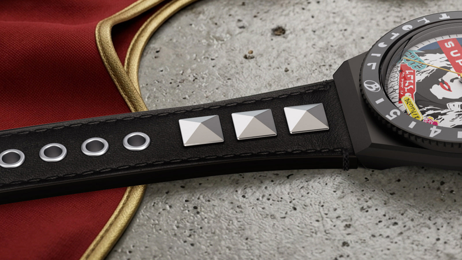 Black leather watch strap with silver pyramid studs, shown alongside a red cape-inspired fabric detail. The edge of the Supergirl x Blondie Q Timex watch case is visible.