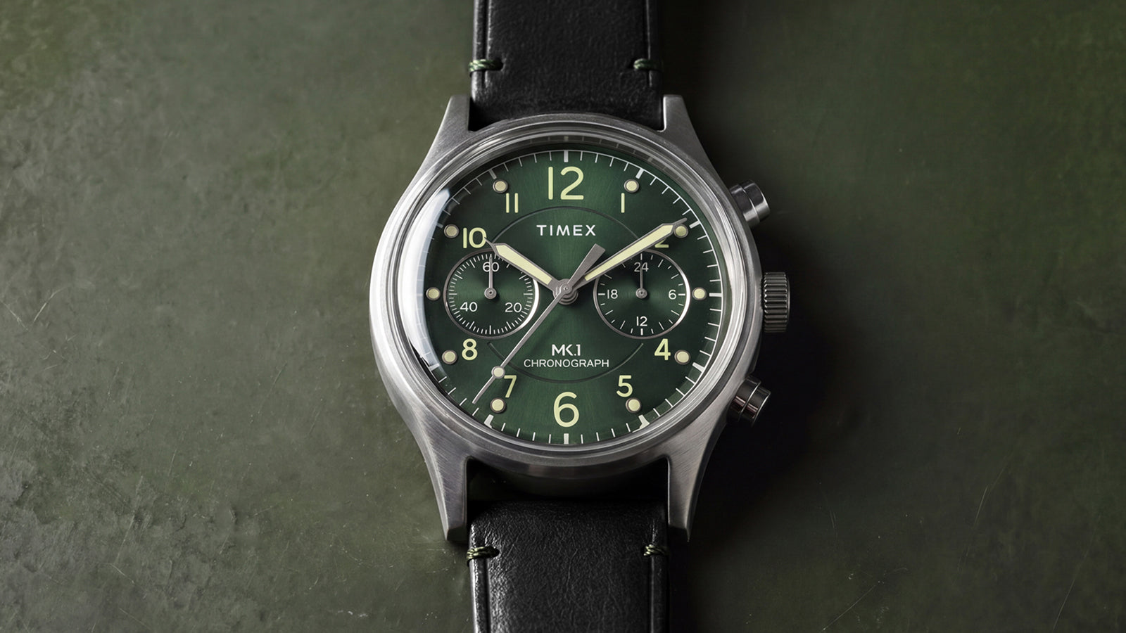 Close-up of the Timex MK1® Chronograph featuring a green dial, chronograph subdials, brushed stainless steel case, and black leather strap.