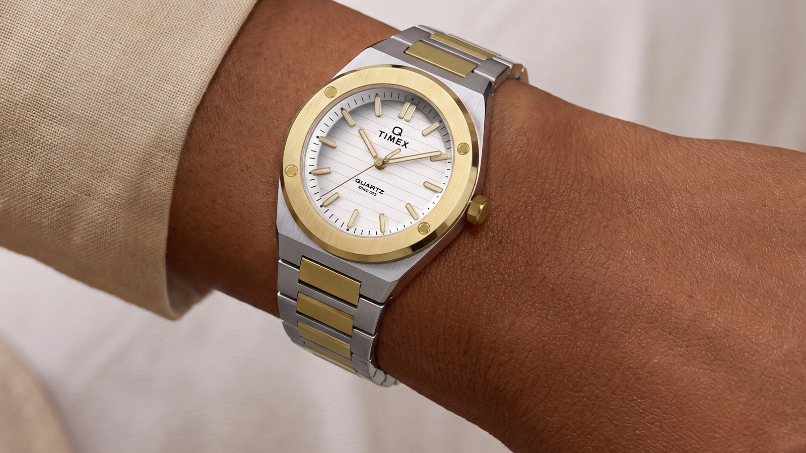 Two-tone Q Timex Marbella watch with a silver and gold-tone stainless steel integrated bracelet, featuring a white textured dial with gold-tone hands and markers, worn on the wrist.