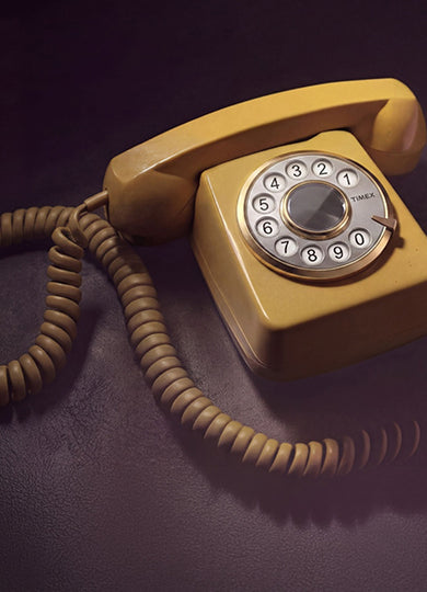 Teléfono antiguo de disco con un dial de la marca Timex expuesto sobre una superficie oscura, con un cable en espiral y una cálida iluminación retro.